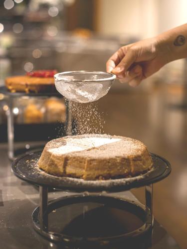 a person is sprinkling powdered sugar on a cake at I Portici Hotel Bologna in Bologna