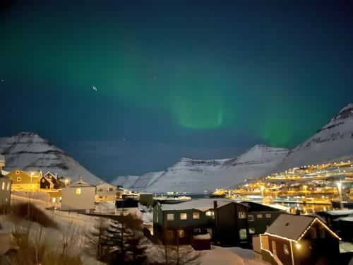 a city with buildings and snow covered mountains at night at Cozy apartment in Klaksvík