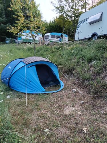 a blue tent sitting in a field next to two rvs at Wild Camping Albareto in Albareto