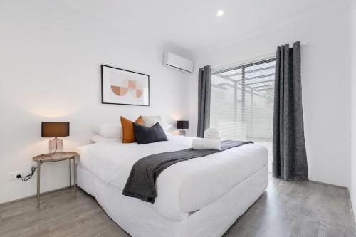 a white bedroom with a large bed and a window at Living luxe in Yokine - King bed and FREE parking in Perth