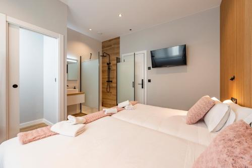 a bedroom with a large white bed with a tv on the wall at White Tree By Arca Hostel in O Pedrouzo