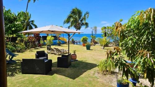 a patio with an umbrella and chairs and the ocean at MOOREA - Fare Nihei in Maharepa