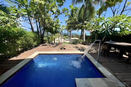 ein Swimmingpool in einem Resort mit dem Meer im Hintergrund in der Unterkunft LC Casas de Praia Jardim dos Guajirus in Tamandaré