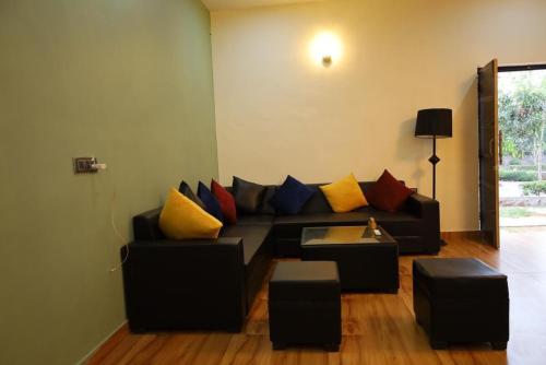 a living room with a black couch with colorful pillows at Niladri farms in Bhundsi