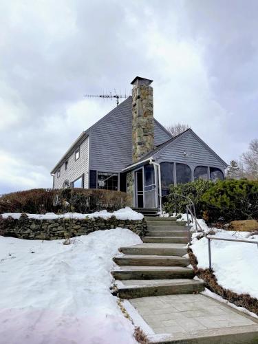 a house with a stone chimney and stairs in the snow at 5H Charming Hilltop Farmhouse with Stunning Views & Modern Comforts Near Mountain View Grand Resort in Whitefield