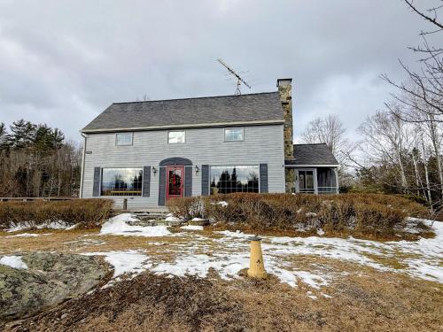 a gray house with a red door in the snow at 5H Charming Hilltop Farmhouse with Stunning Views & Modern Comforts Near Mountain View Grand Resort in Whitefield