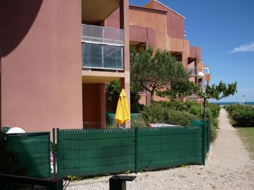 a building with a green fence and an umbrella at Barcarès F2 cabine, RDC, plage 50 m, 28 m2, 6 personnes in Le Barcarès