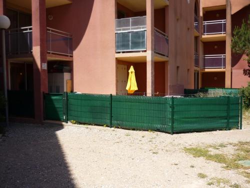 une clôture verte devant un bâtiment avec un parapluie jaune dans l'établissement Barcarès F2 cabine, RDC, plage 50 m, 28 m2, 6 personnes, au Barcarès