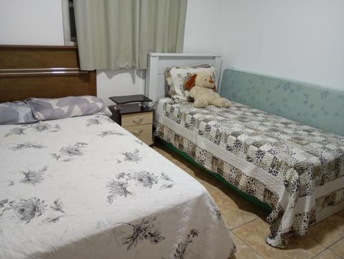a bedroom with two beds and a teddy bear sitting on a bench at Casa de praia a 100 metros da praia in Passo de Torres