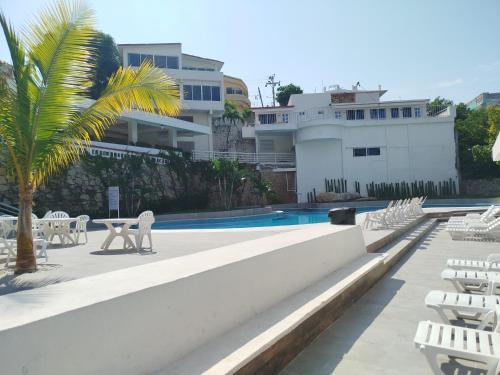 a pool with chairs and a table and a palm tree at Hotel Aristos Acapulco in Acapulco