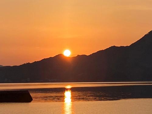 a sunset over the water with a mountain in the background at しまなみ海道 COTTAGE Umimae in Onomichi