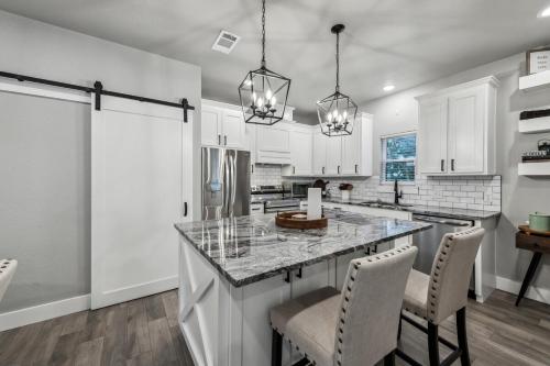 a kitchen with white cabinets and a large island with chairs at Mins to Granbury Med Ctr, Mins to Lake, Firepit, Stunning Modern Kitchen in Granbury