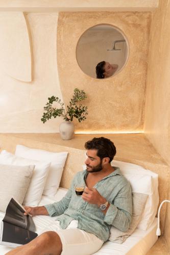 a man sitting on a bed with a laptop and a mirror at Heyday Luxury Suites in Perissa