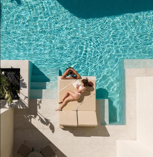 a woman laying on a chair next to a swimming pool at Heyday Luxury Suites in Perissa