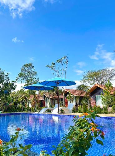 a swimming pool with a blue umbrella and chairs at The Lake Farm - Dak Lak in Buon Ma Thuot