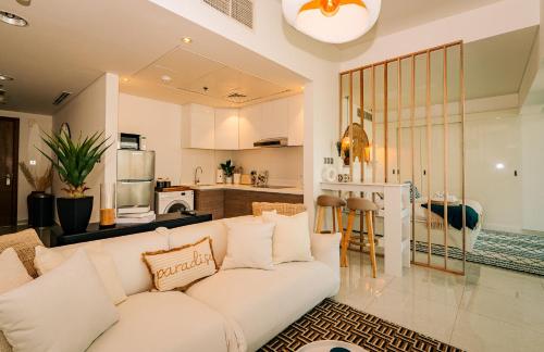 a living room with a white couch and a kitchen at Studio In Al Hadeel Hosted By Voyage in Abu Dhabi