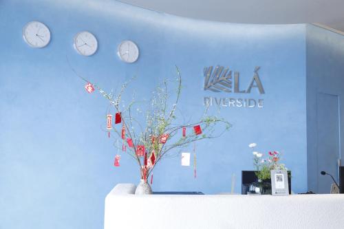 a blue wall with clocks and a vase with a plant at Lá Riverside Boutique Hotel in Mỹ Phước