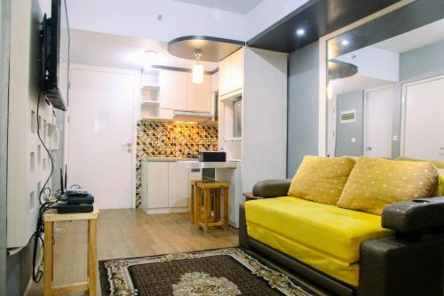 a living room with a yellow couch and a kitchen at Modern Furnished 3BR at Springlake Summarecon Bekasi Apartment By Travelio in Bekasi