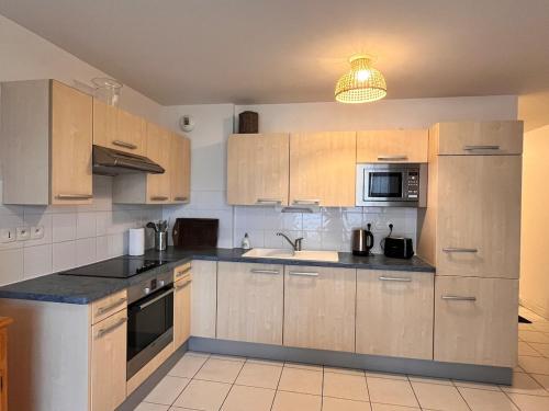 une cuisine avec des placards en bois et des comptoirs noirs dans l'établissement Escapade à deux pas de la mer parking privé, à Merlimont