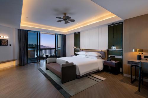 a bedroom with a bed and a desk and a balcony at Sanya Golden Phoenix Seaview Hotel in Sanya