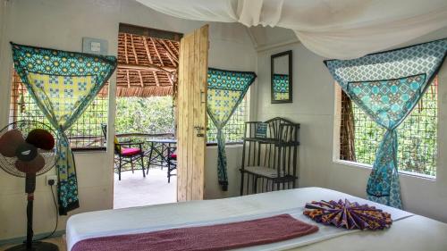 a bedroom with a bed and a room with windows at Stilts Diani Beach in Diani Beach
