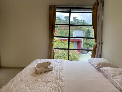 a bed with a stuffed animal sitting on it in front of a window at Family Only Cozy Villa on Top of Bandung - De Reiz Iris Syariah 4BR in Ciburial