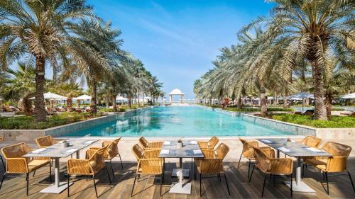 a pool with tables and chairs and palm trees at Rixos Al Mairid Ras Al Khaimah - Ultra All Inclusive in Ras al Khaimah