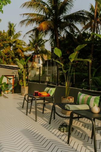 a patio with chairs and tables and palm trees at Minimalist Panjim in Panaji