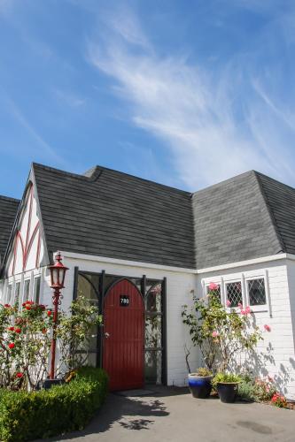 a white house with a red door and some flowers at Camelot Motor Lodge in Christchurch