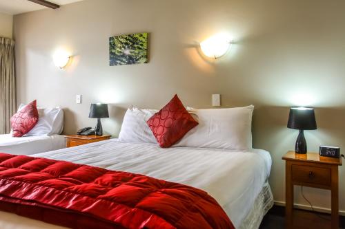 a bedroom with two beds with red and white pillows at Camelot Motor Lodge in Christchurch