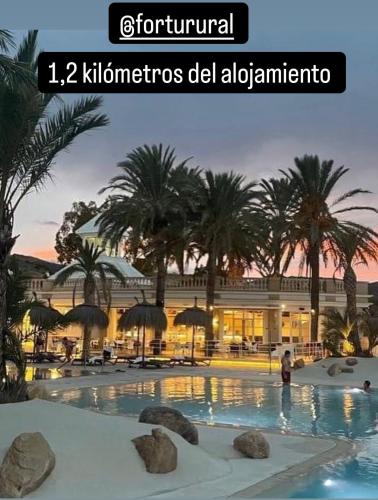 a resort swimming pool with palm trees and a building at Apartamento Rural Casa Cueva in Murcia