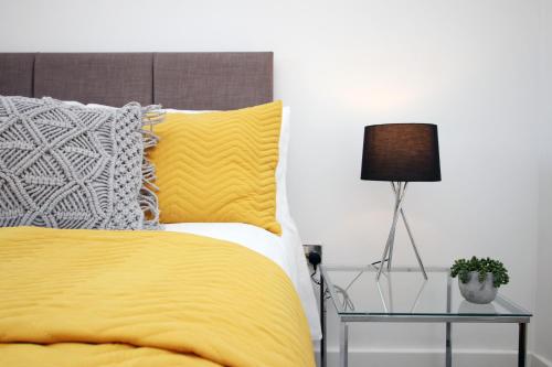 a bed with yellow sheets and a lamp on a table at Dray Court - Hyper Central 2 Bedroom Apartment in Cardiff