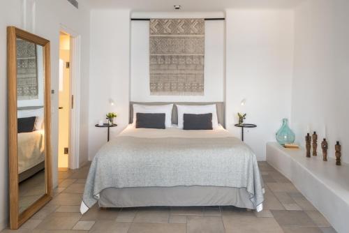 a white bedroom with a bed and a mirror at Porto Fira Suites in Fira