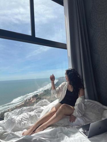 a woman sitting on a bed in front of a window at Apec Mandala Mũi Né - Phan Thiết in Phan Thiet
