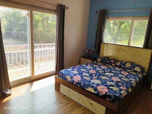 a bedroom with a bed with a floral comforter and two windows at Huvazeel Villa - Murbad for Monthly rental only in Saralgaon