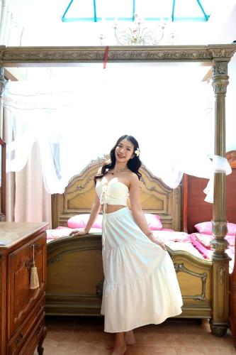 a woman in a white dress standing in front of a bed at Paris De Floor Khaoyai in Pak Chong