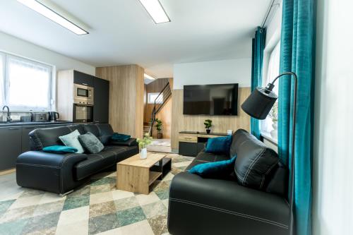 a living room with two black leather couches and a tv at Mátravölgy Apartmanház in Pásztó
