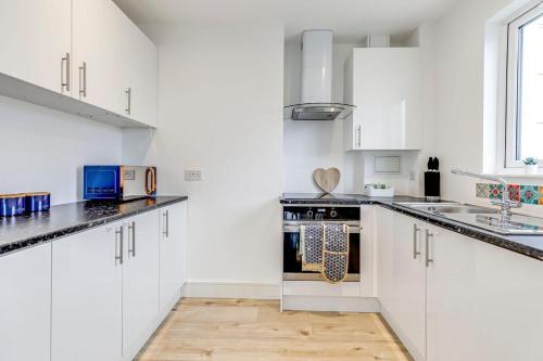 a white kitchen with black countertops and white cabinets at Prime location, Panoramic city views, Surround Balcony Near Train Stn - Central Luton in Luton