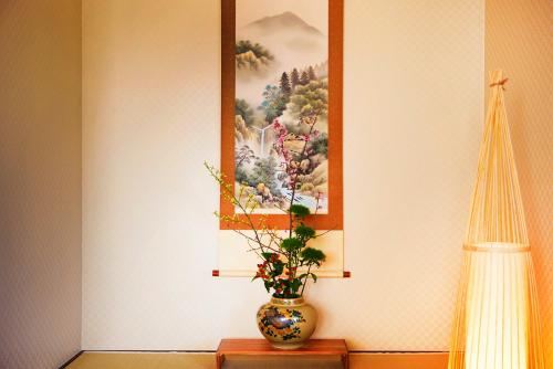 a vase sitting on a table with a painting on the wall at 鎌倉小町 大仏さまノ休日ホテル The Big Buddha Holiday Hotel Kamakura in Kamakura
