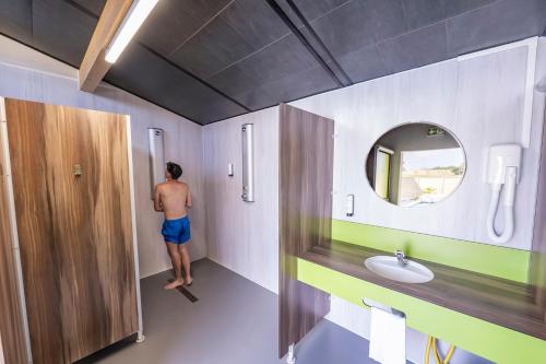un homme debout dans une salle de bains avec un miroir dans l'établissement Camper au Moulin de la brevette, à Arbigny