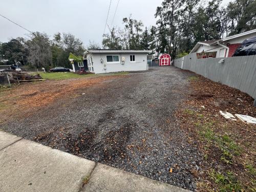 an empty driveway with a white house and a fence at Little Italy - Welcome to Venice Tiny House in Jacksonville