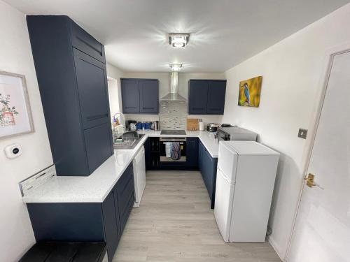 a kitchen with blue cabinets and a white refrigerator at Riverside 2 Bedroom Townhouse with Car Charger in Abergavenny