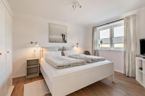 a white bedroom with a bed and a window at Ferienhaus Waterkant mit Hund in Klanxbüll