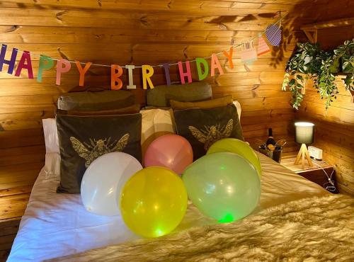 a bunch of balloons on a bed with a happy birthday banner at Loch Lomond Hideaways- Luxury Cabins with Jacuzzis in Drymen