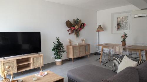 a living room with a flat screen tv and a table at "LES ALIZES" Côté jardin Proche Bord de mer in Saint-Raphaël