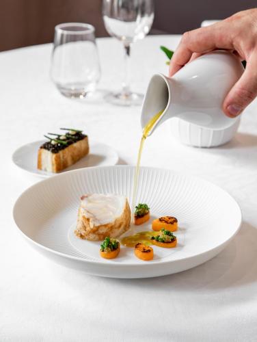 a person pouring sauce onto a plate of food at La Cour des Consuls Hotel & Spa Toulouse - MGallery Collection in Toulouse