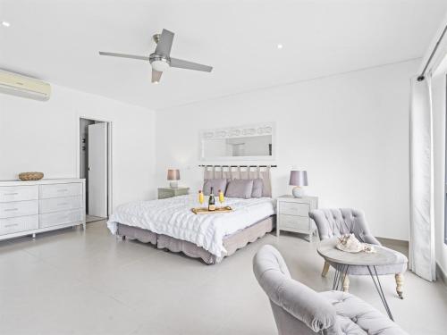 a white bedroom with a bed and two chairs at Beacon Hill Hideaway Luxury Condo in Simpson Bay in Simpson Bay