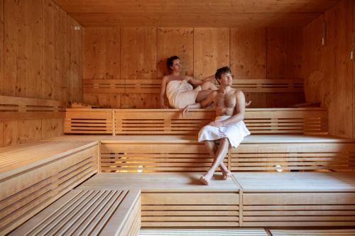 a woman and a man sitting in a sauna at Hotel Terme Antico Bagno in Pozza di Fassa