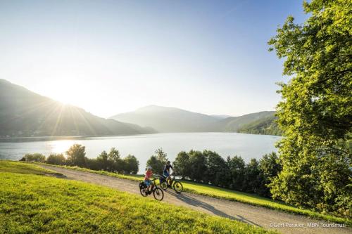 two people riding bikes on a path next to a lake at Pension Sedlak in Millstatt