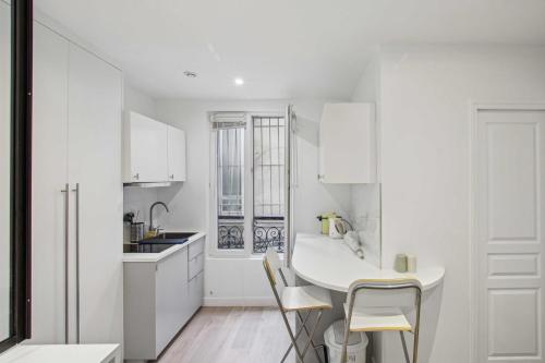 - une cuisine blanche avec des placards blancs, une table et des chaises dans l'établissement Le Petit cosy de Montmartre, à Paris